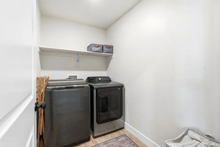 Laundry area featuring a wall-mounted shelf, light-toned walls, and wood-finish flooring