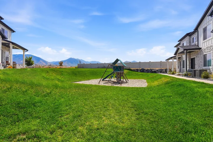 Expansive green space featuring a play structure on a gravel base, surrounded by residential buildings with stone and siding exteriors