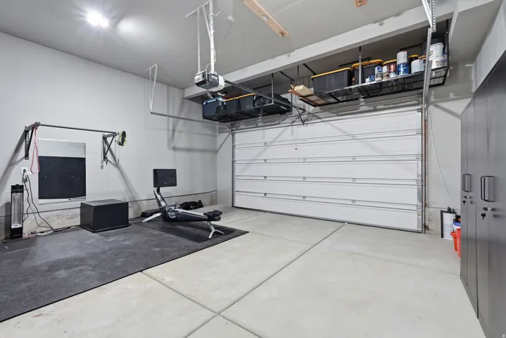 Concrete flooring, bright overhead lighting, built-in overhead storage racks, an automatic garage door opener, and a wall-mounted storage cabinet