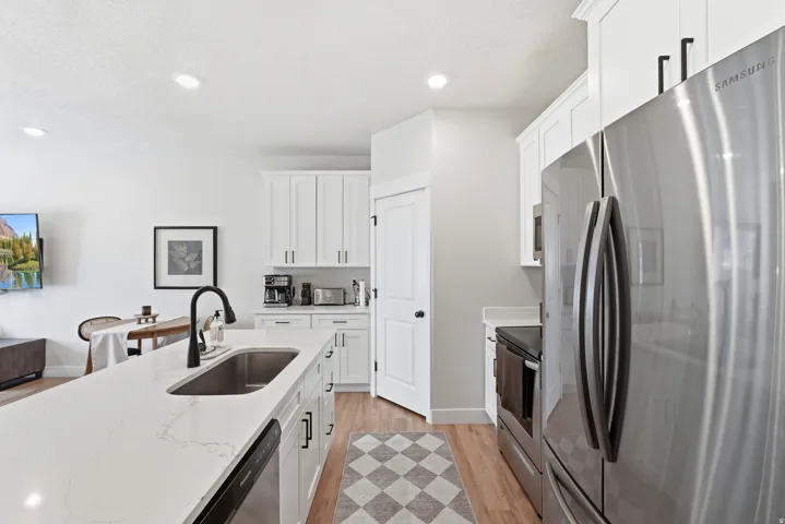 Modern kitchen with white cabinetry, stainless steel appliances, a large island with an undermount sink, and wood-finish flooring