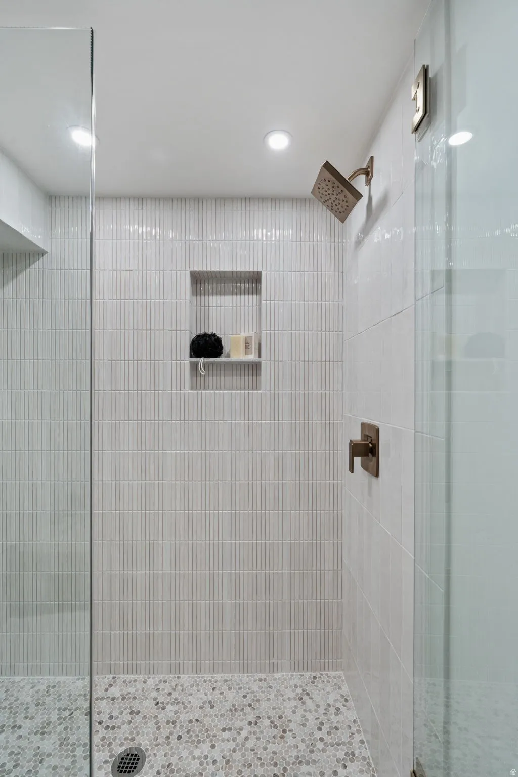 Glass-enclosed shower featuring vertical tile, a recessed niche, a rain shower head, and a mosaic tile floor