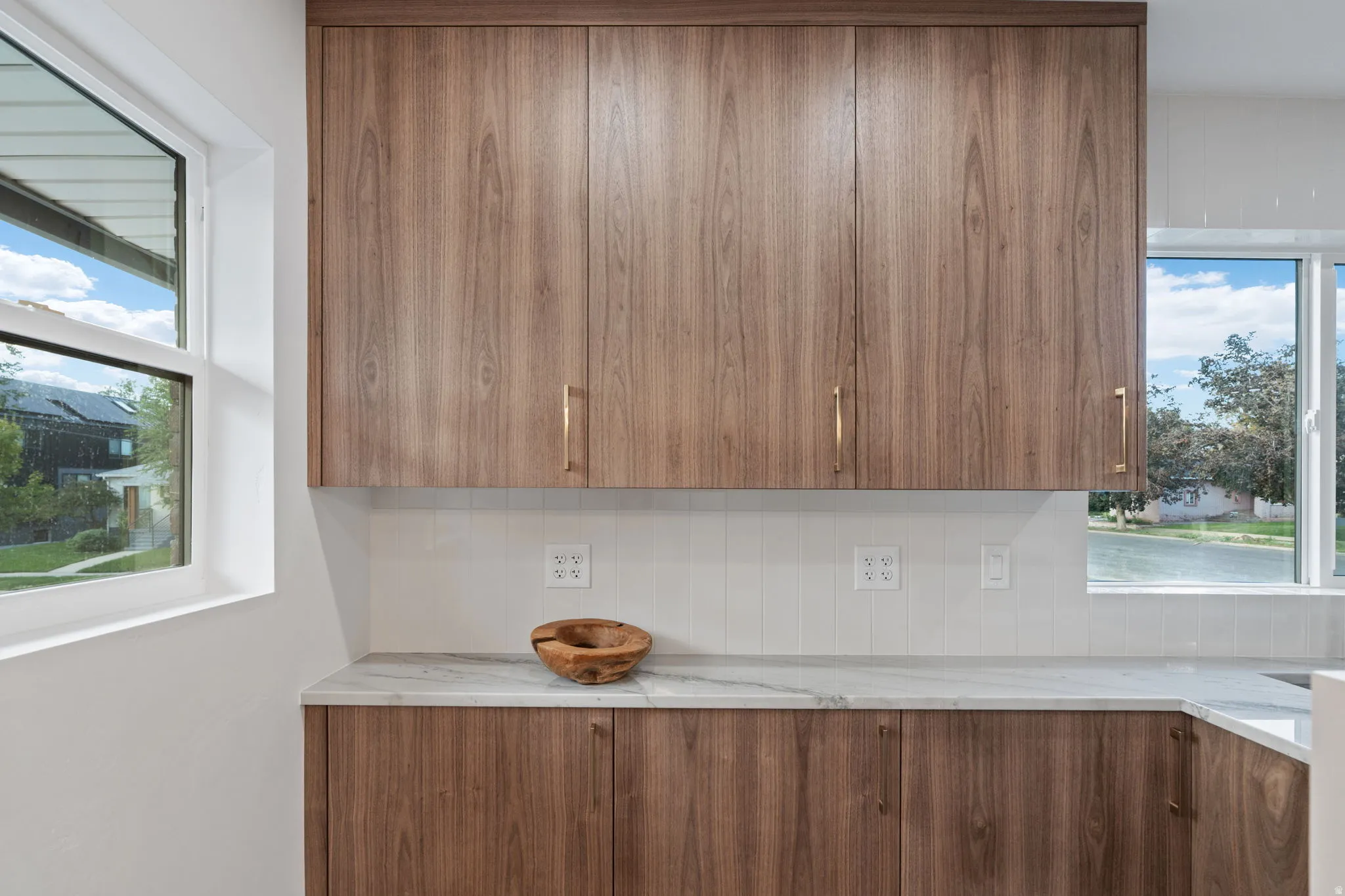 Wood-finish cabinetry with golden hardware, white tile backsplash, and light-toned countertop