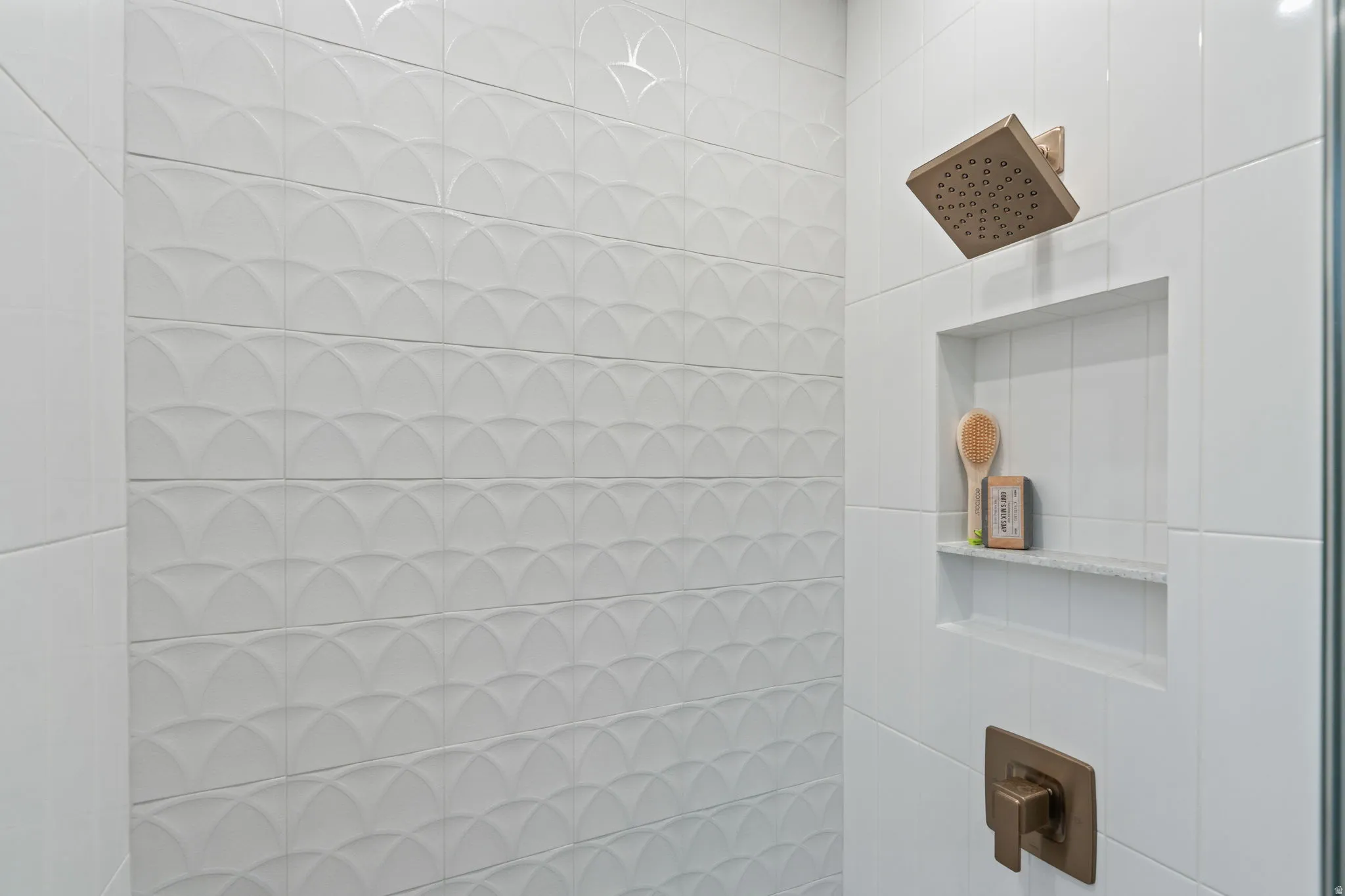 White tiled shower with textured accent wall, integrated shower niche with stone shelf, and bronze-finish fixtures