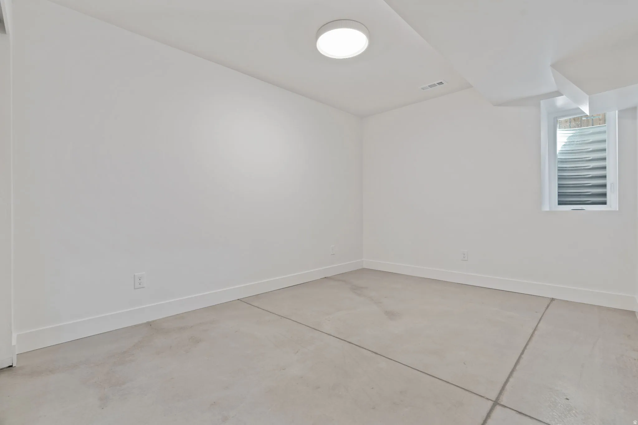 Recessed ceiling light, white painted walls, concrete flooring with expansion joints, window with well, and white trim