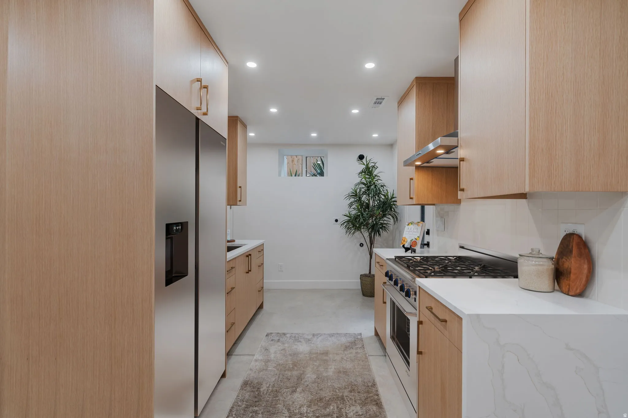 Galley kitchen featuring light wood-finish cabinetry, stainless steel appliances, white countertops, a gas range with an exhaust hood, and recessed lighting