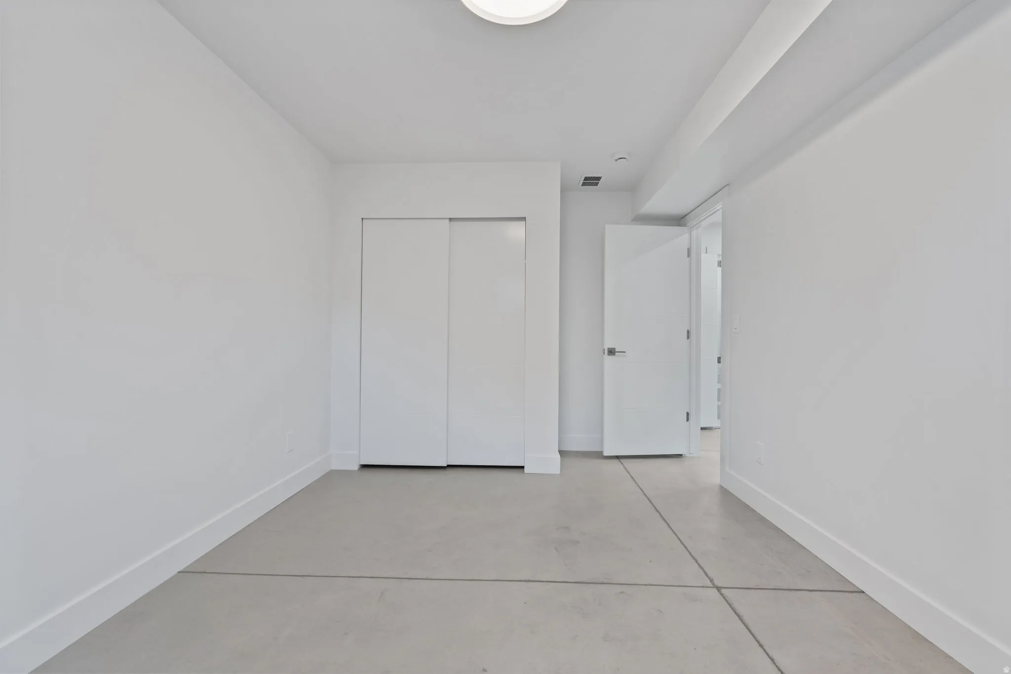 Concrete flooring, white walls, white sliding closet doors, white door, and recessed lighting