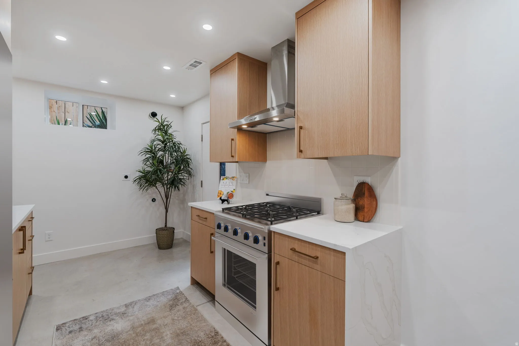 Kitchen featuring light wood-finish cabinetry, stainless steel range with matching hood, white countertops, and recessed lighting