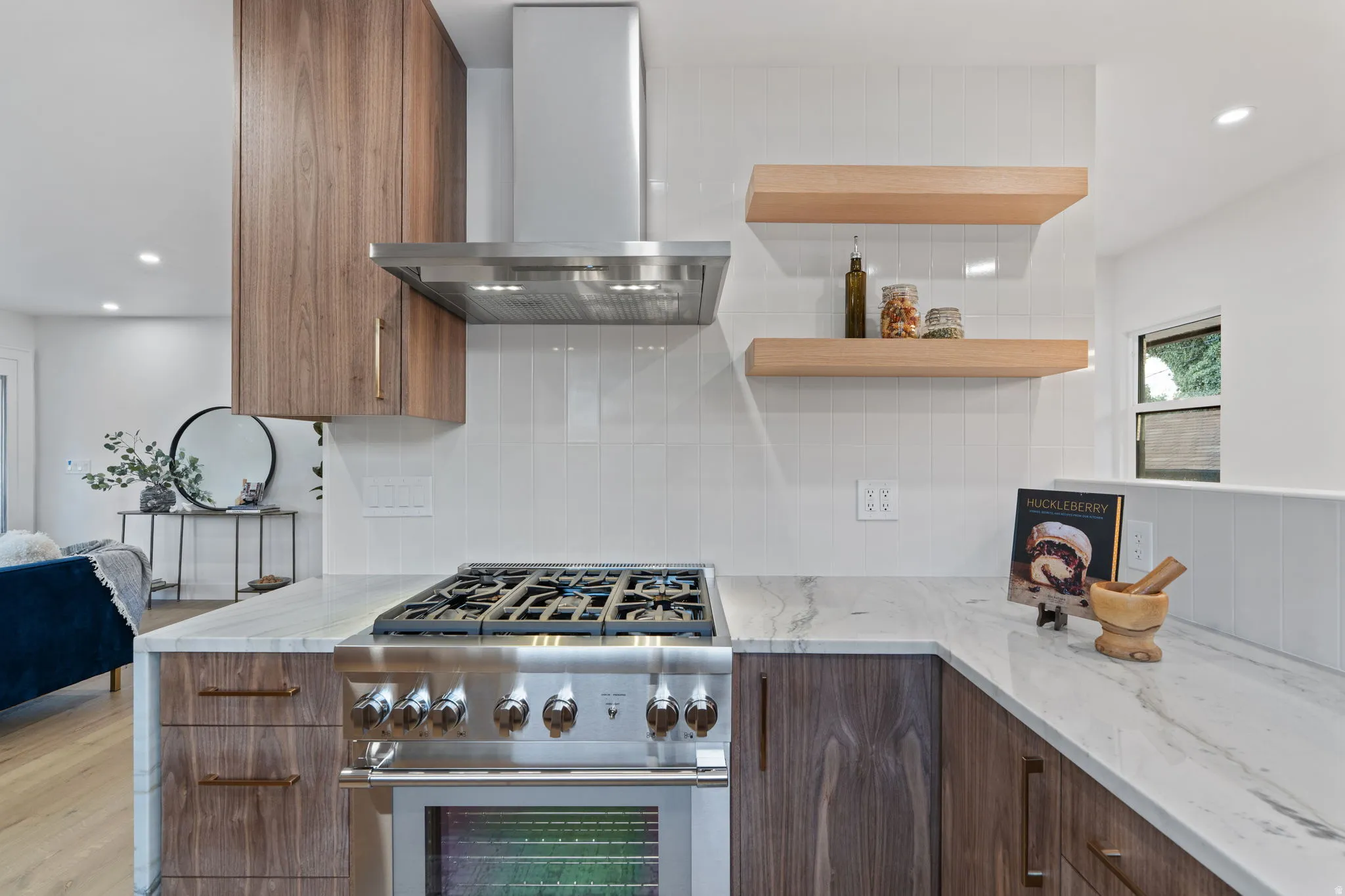 Gourmet kitchen featuring a stainless steel range and hood, wood-finish cabinetry, floating wood shelves, and light-toned countertops