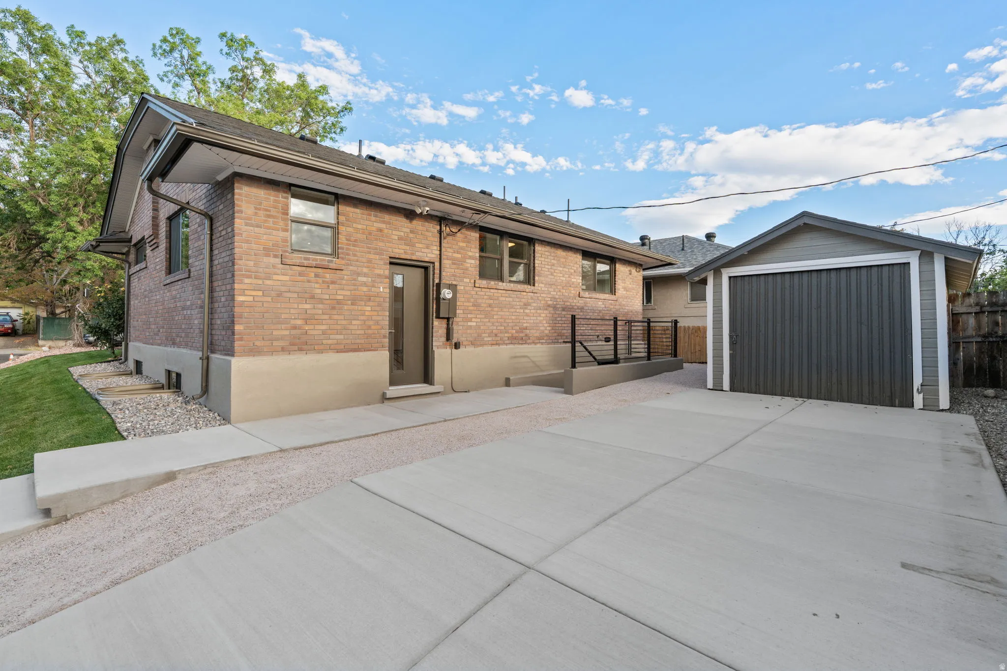 Brick exterior, concrete driveway, detached garage with metal siding, gravel landscaping, and black metal railing