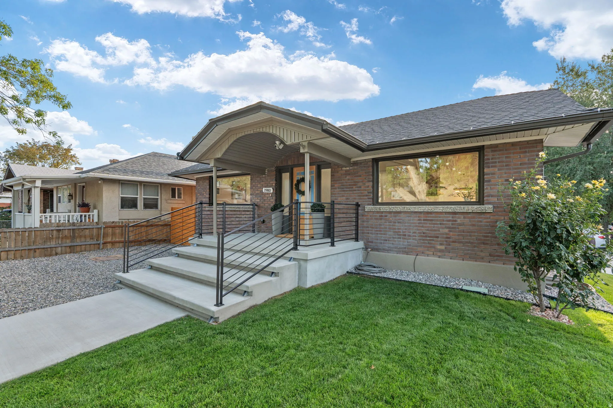 Brick exterior, covered front entry, concrete steps with metal railings, asphalt shingle roof, and a manicured lawn
