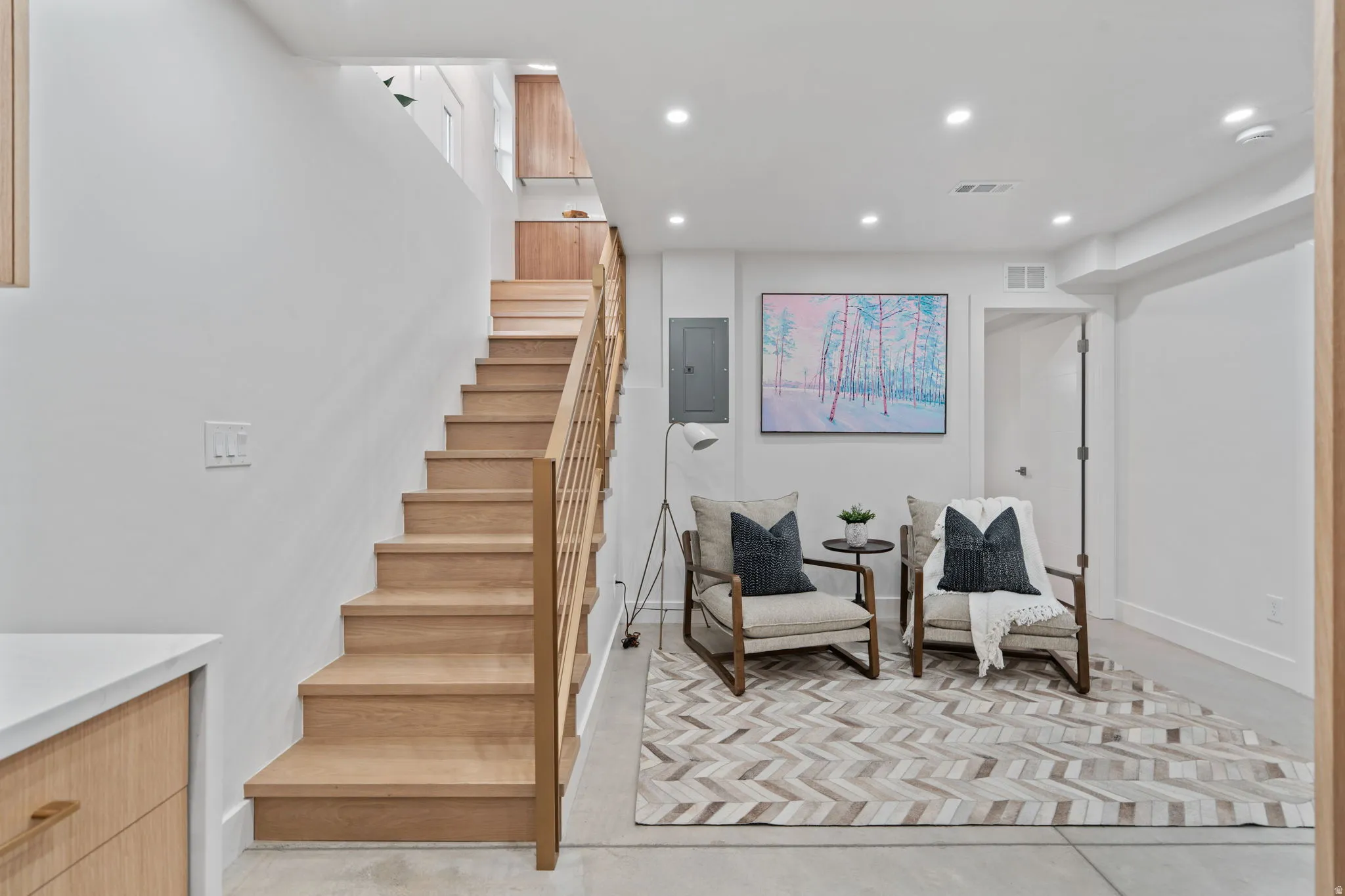Hardwood staircase with natural wood railing, recessed ceiling lighting, light wood-finish cabinetry, and white walls
