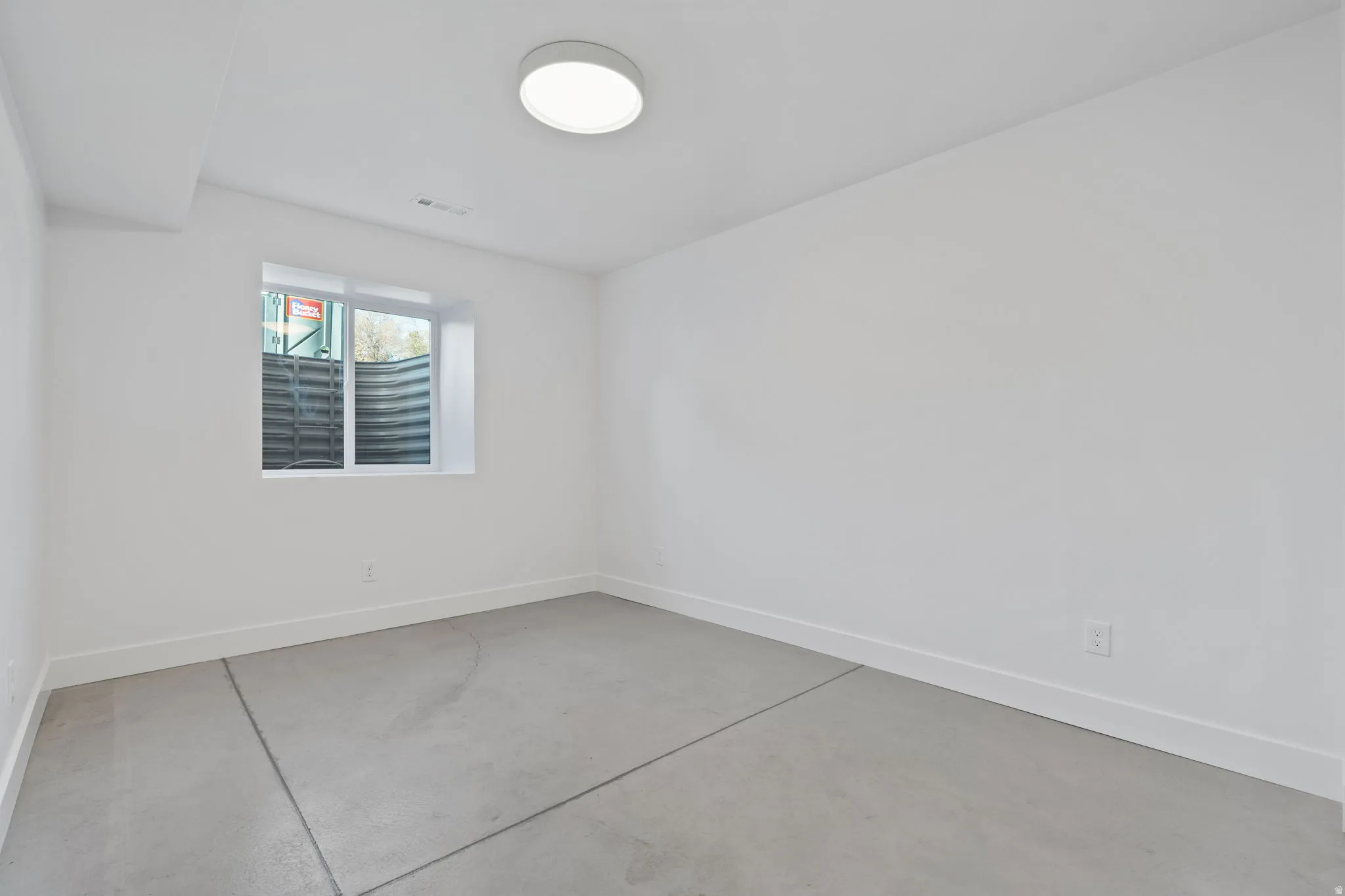 Smooth concrete flooring, white painted walls, single window, flush-mount ceiling light