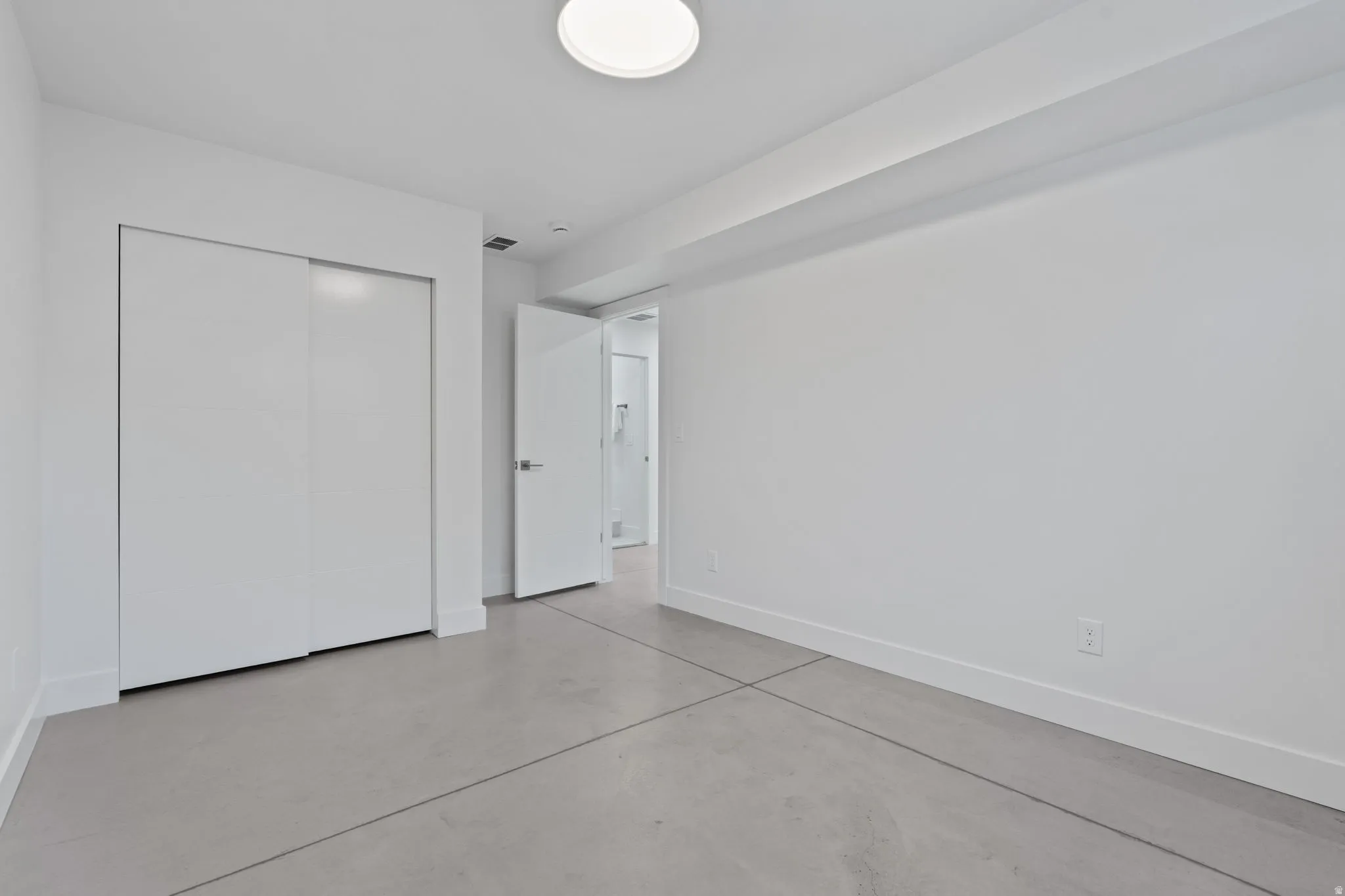 Smooth concrete flooring, white walls, and a flush-mount ceiling light