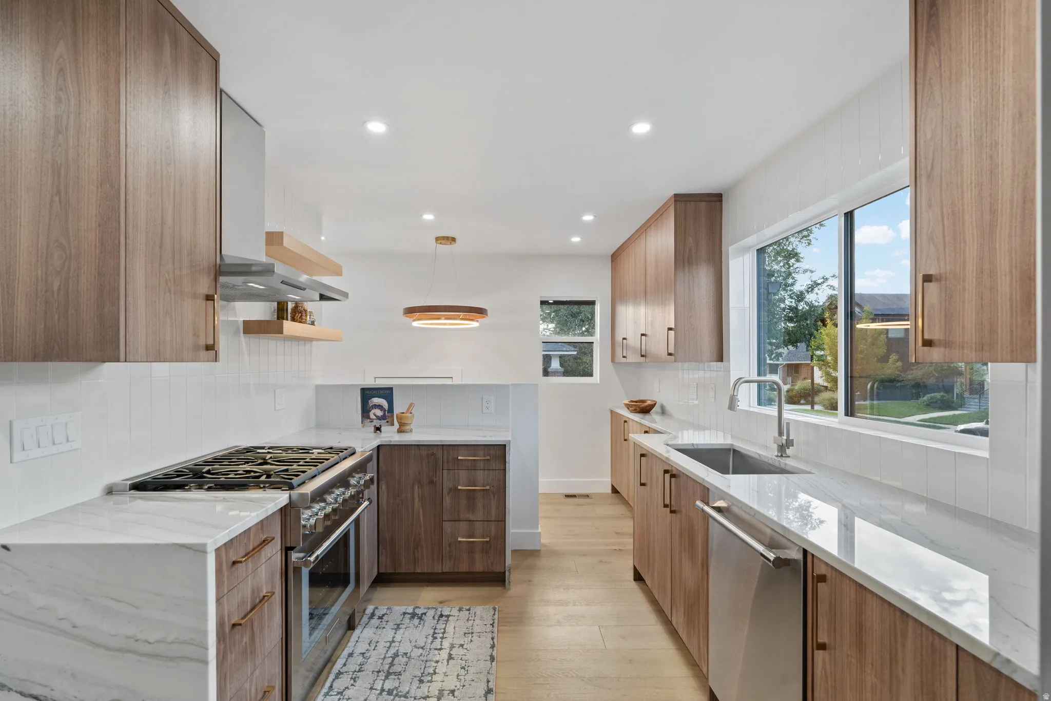 Galley kitchen featuring wood-finish cabinetry, stainless steel appliances, white subway tile backsplash, light wood-finish flooring, and white countertops