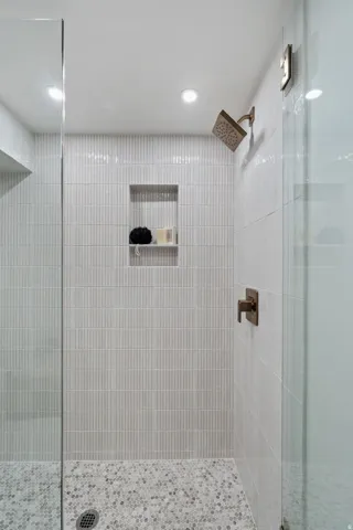 Glass-enclosed shower featuring vertical tile, a recessed niche, a rain shower head, and a mosaic tile floor
