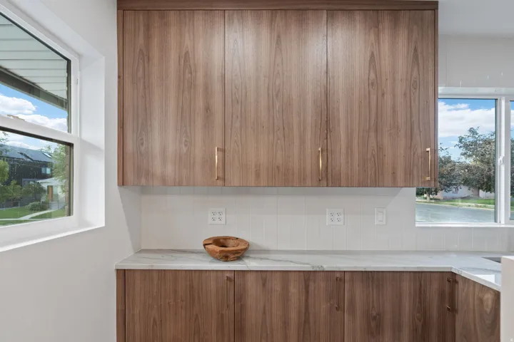 Wood-finish cabinetry with golden hardware, white tile backsplash, and light-toned countertop