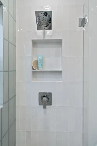 White tiled shower featuring a built-in niche, square rain shower head, and polished chrome fixtures