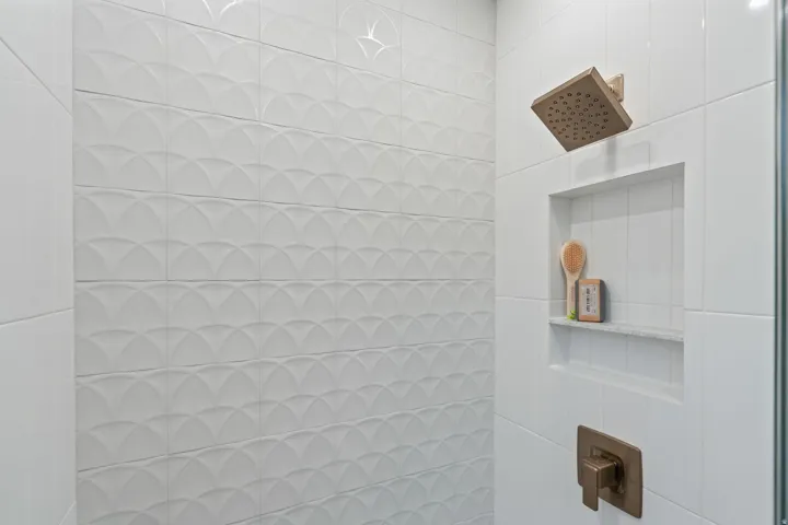 White tiled shower with textured accent wall, integrated shower niche with stone shelf, and bronze-finish fixtures