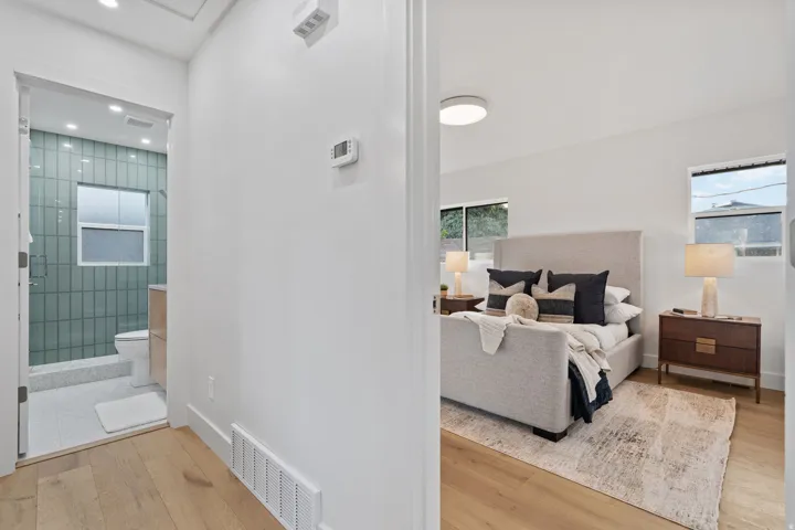 Wood-finish flooring throughout, bright white wall finishes, recessed lighting, and a bathroom featuring vertical tile and a glass-enclosed shower