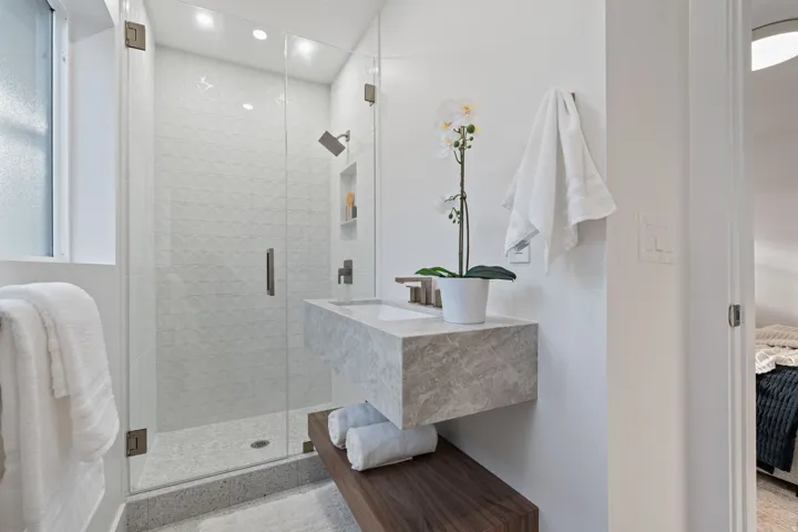 Floating vanity with integrated sink, glass-enclosed shower, wall-mounted faucet, and wood-finish accent shelf