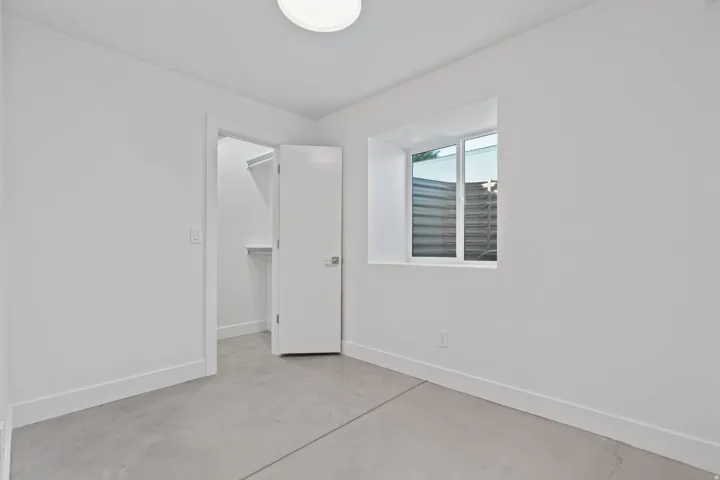 Recessed window with exterior well, overhead flush mount lighting, solid core door, and concrete flooring