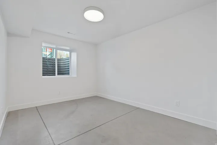 Smooth concrete flooring, white painted walls, single window, flush-mount ceiling light