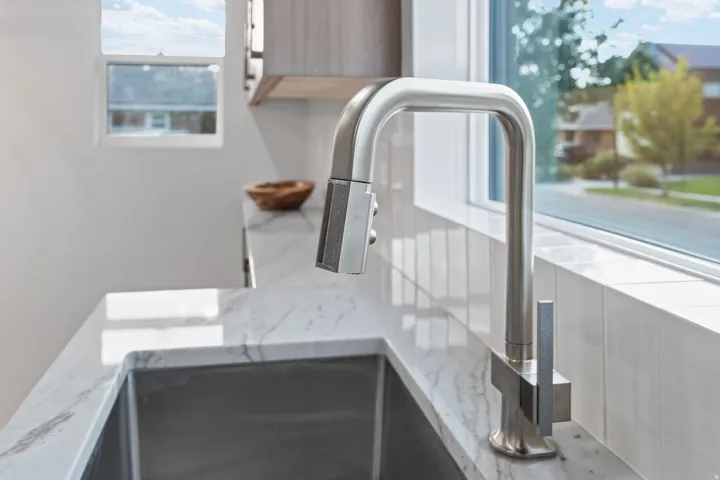 Stainless steel pull-down faucet, undermount sink, stone-finish countertop, and tile backsplash