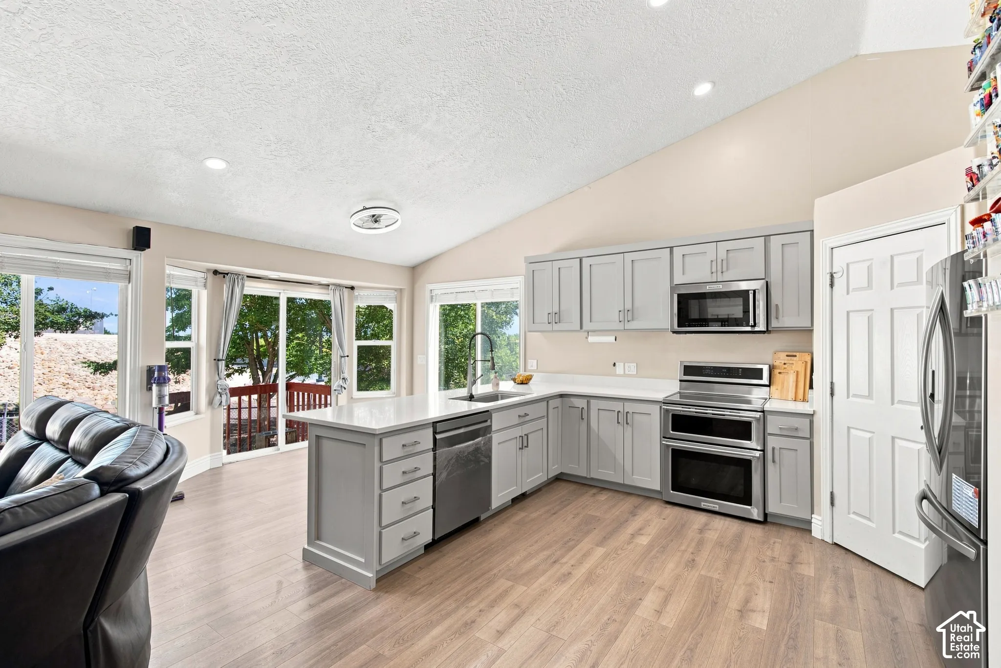 Vaulted ceiling kitchen with light gray cabinetry, stainless steel appliances, white countertops, and wood-finish flooring