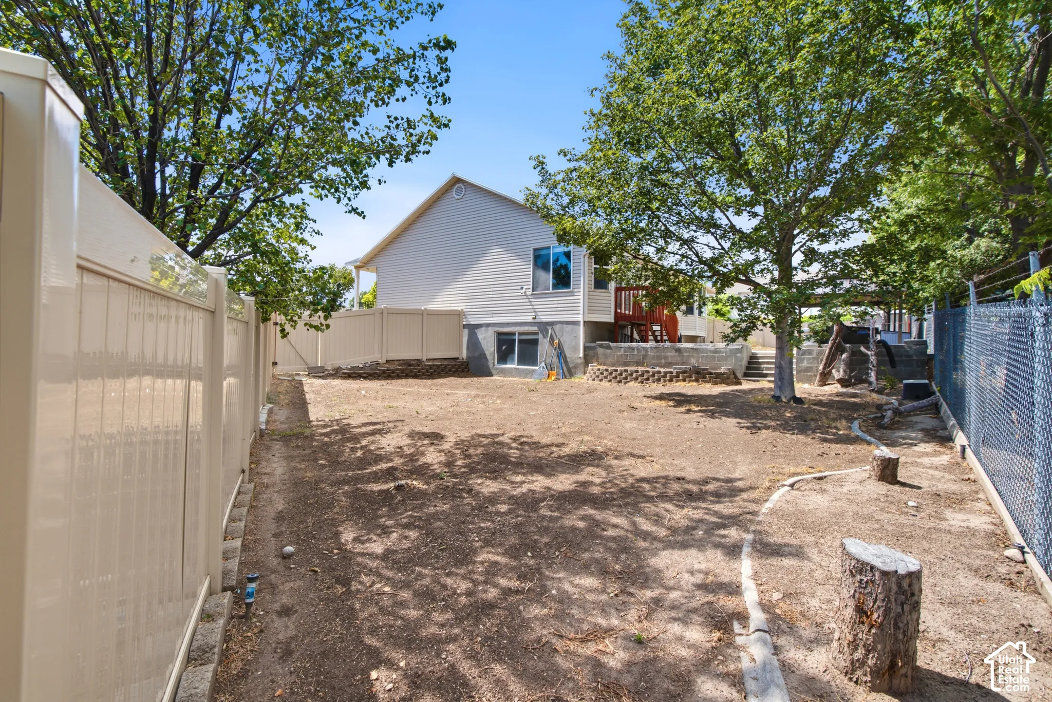 Expansive backyard featuring a privacy fence, mature trees, and a retaining wall