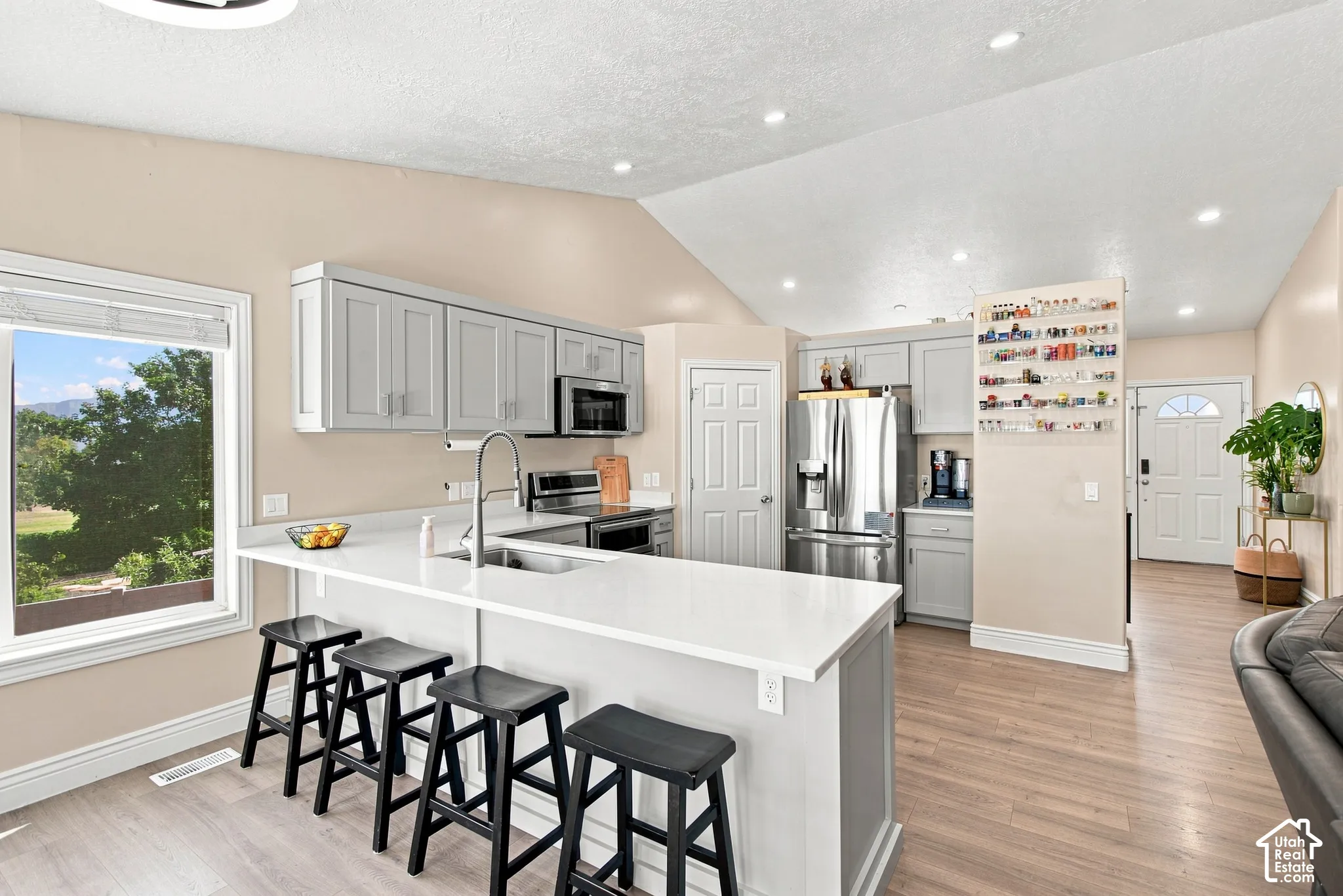 Spacious kitchen featuring an expansive island with seating, integrated sink with gooseneck faucet, light wood-finish flooring, and stainless steel appliances