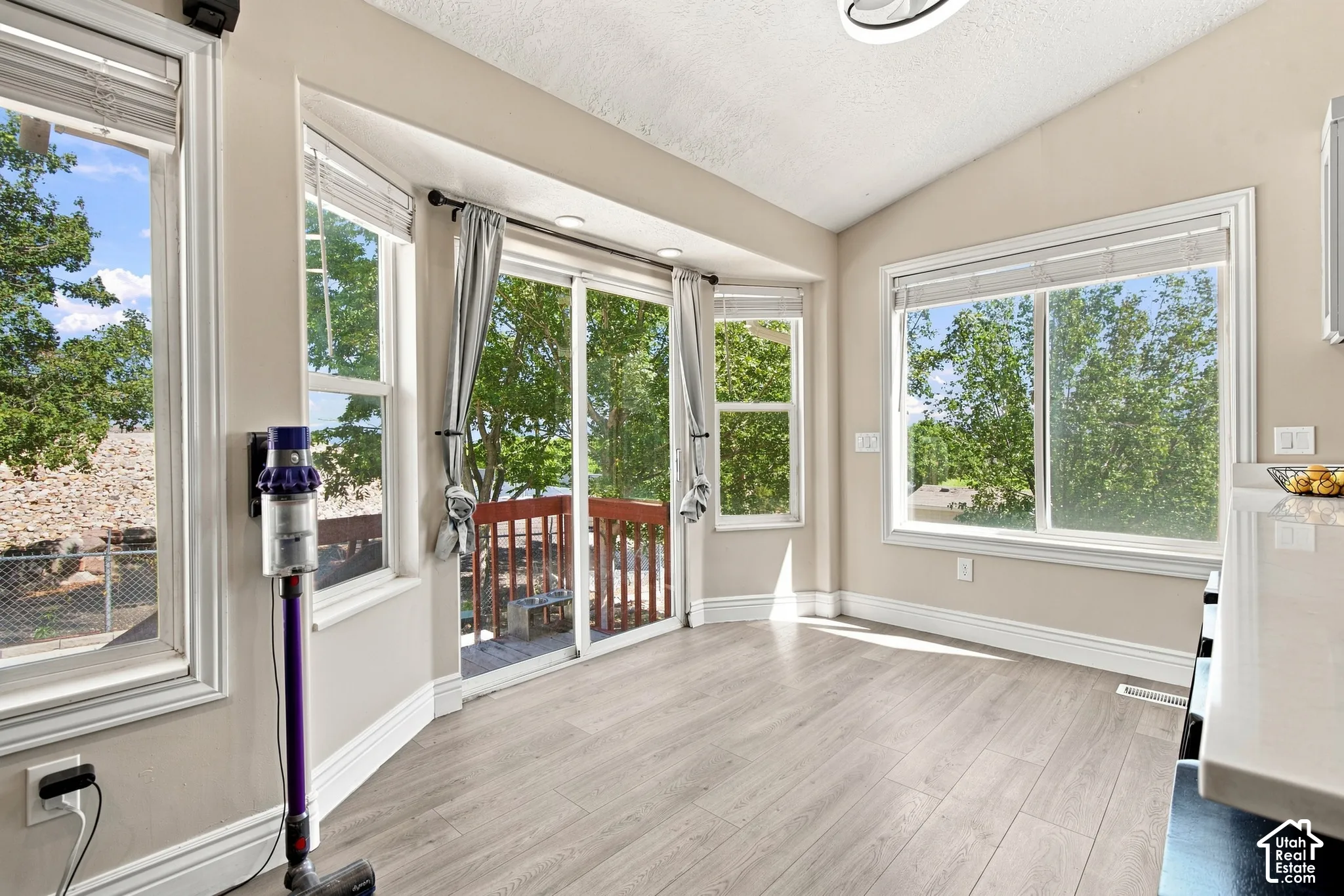 Bright sunroom with abundant natural light from multiple large windows and glass doors overlooking mature landscaping