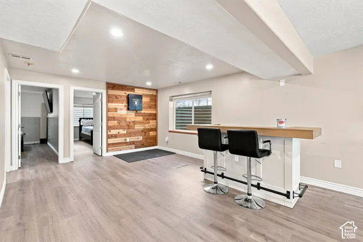 Built-in bar with a wood-finish countertop, wood-finish accent wall, recessed lighting, and wood-finish flooring