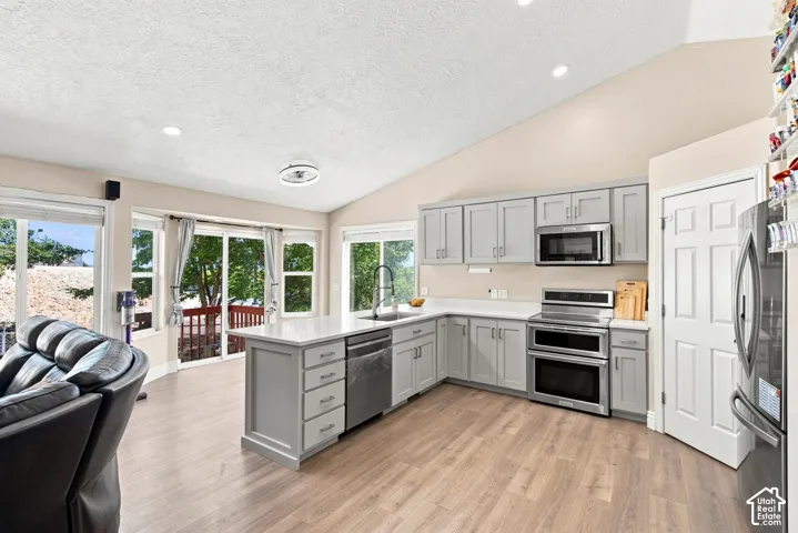 Vaulted ceiling kitchen with light gray cabinetry, stainless steel appliances, white countertops, and wood-finish flooring