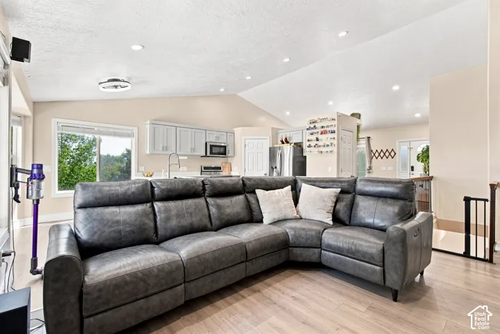 Open-concept living area featuring a sectional layout with wood-finish flooring, recessed ceiling lighting, and abundant natural light from large multi-pane windows