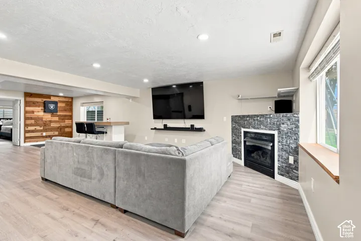 Light wood-finish flooring, recessed lighting, built-in fireplace with stone surround, wood accent wall, and a built-in bar