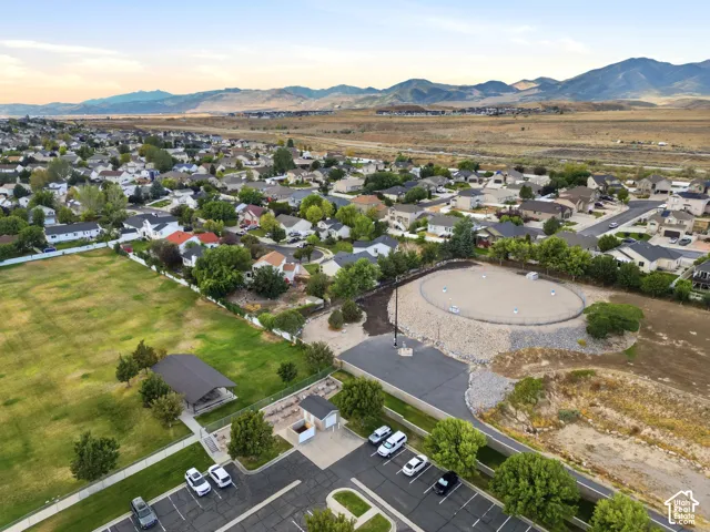 Expansive neighborhood setting with residential structures, a large green field, and distant mountains