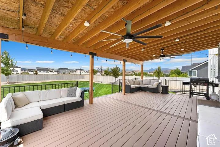 Expansive covered deck featuring composite decking, exposed wood beam ceiling, multiple ceiling fans, and integrated string lighting