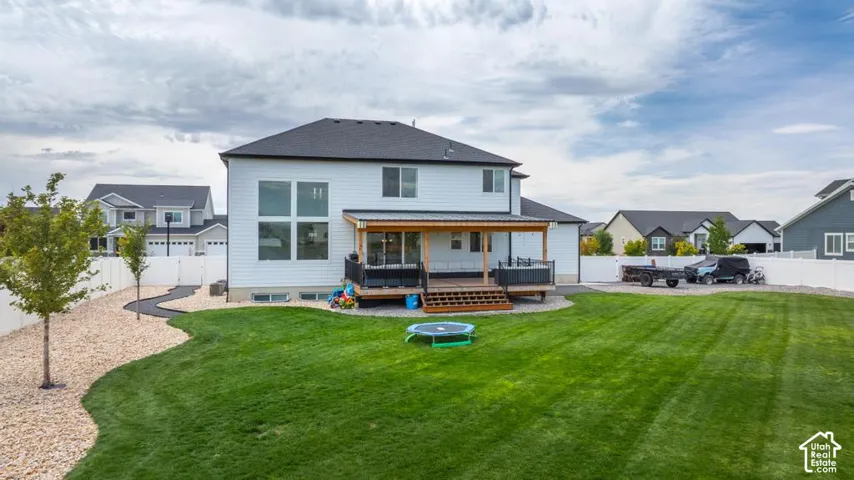 Expansive backyard featuring a manicured lawn, a covered wood-finish deck, and a white privacy fence