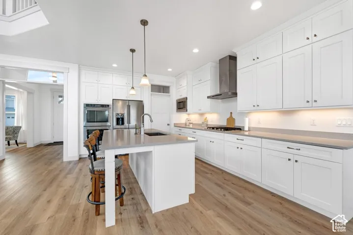 Kitchen featuring white shaker cabinetry, stainless steel appliances, stone countertops, a large island with seating, and wood-finish flooring