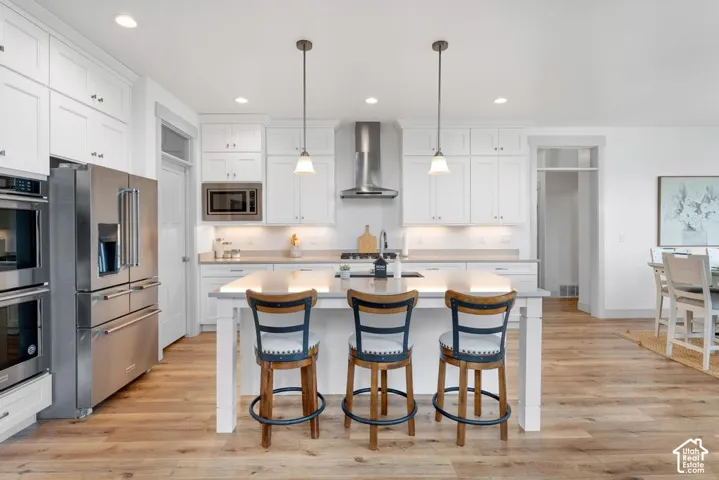 Kitchen with white cabinetry, stainless steel appliances, a center island with pendant lighting, stone countertops, and wood-finish flooring