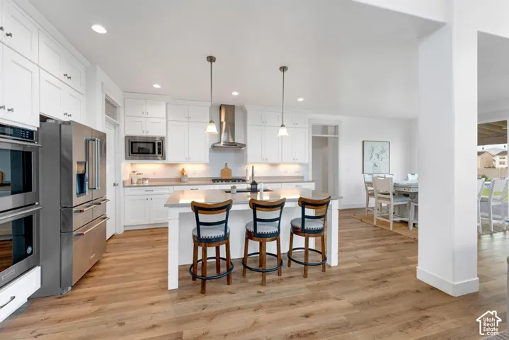 White shaker cabinetry, stainless steel appliances, wood-finish flooring, central island with pendant lighting, and recessed lighting