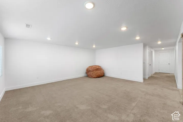 Expansive room with neutral carpet, recessed lighting, white walls, and window with blinds