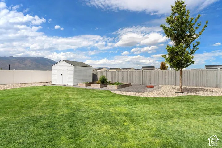 Expansive grassy yard with a storage shed, raised garden beds, established tree, and a gravel accent area