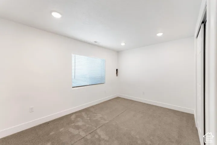 Recessed ceiling lighting, neutral carpet flooring, white walls, and a window with blinds
