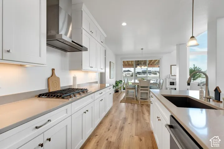 Modern kitchen featuring white cabinetry, light-toned countertops, a stainless steel range hood, and wood-finish flooring