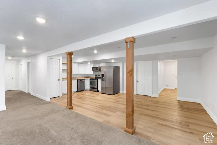 Recessed lighting throughout, wood-finish flooring, white cabinetry, stainless steel appliances, and wood structural pillars