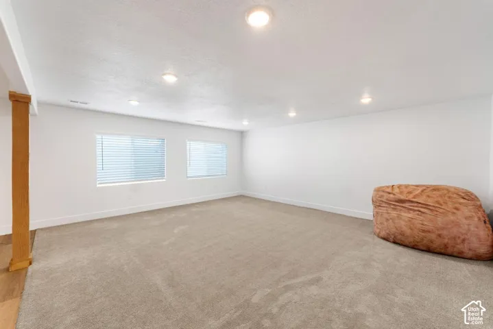 Spacious room featuring recessed lighting, two windows with blinds, plush carpeting, and a wood-finish support column