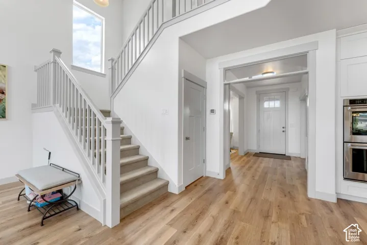 Two-story foyer with wood-finish flooring, carpeted staircase, tall window, and white paneled entry door