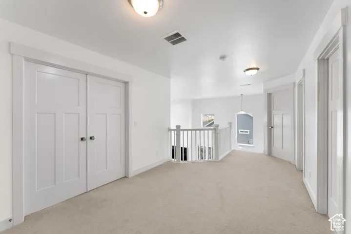 Carpeted hallway featuring white panel doors, recessed lighting, and a white banister