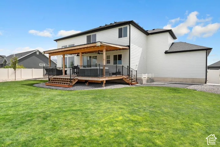 Expansive backyard featuring a covered patio, wooden deck with railing, and a vibrant green lawn